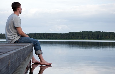 young man sitting on the edge of a dock looking out at calm water on a lake